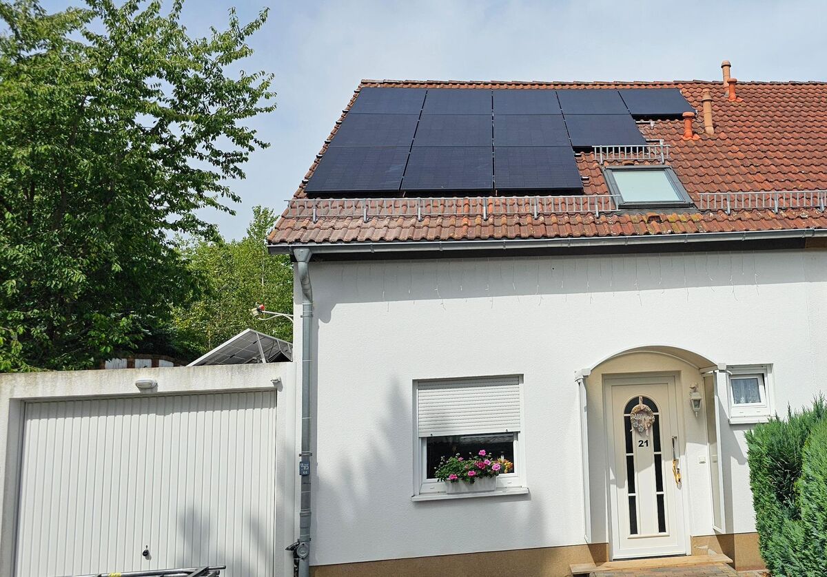 Ein weißes Haus mit Solarpanelen auf dem Dach und einer blühenden Fensterbank.