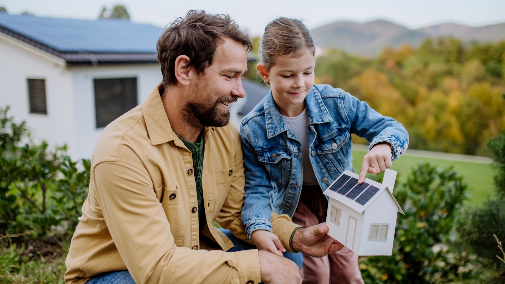Little girl with her dad holding paper model of house with solar panels, explaining how it works.Alternative energy, saving resources and sustainable lifestyle concept.