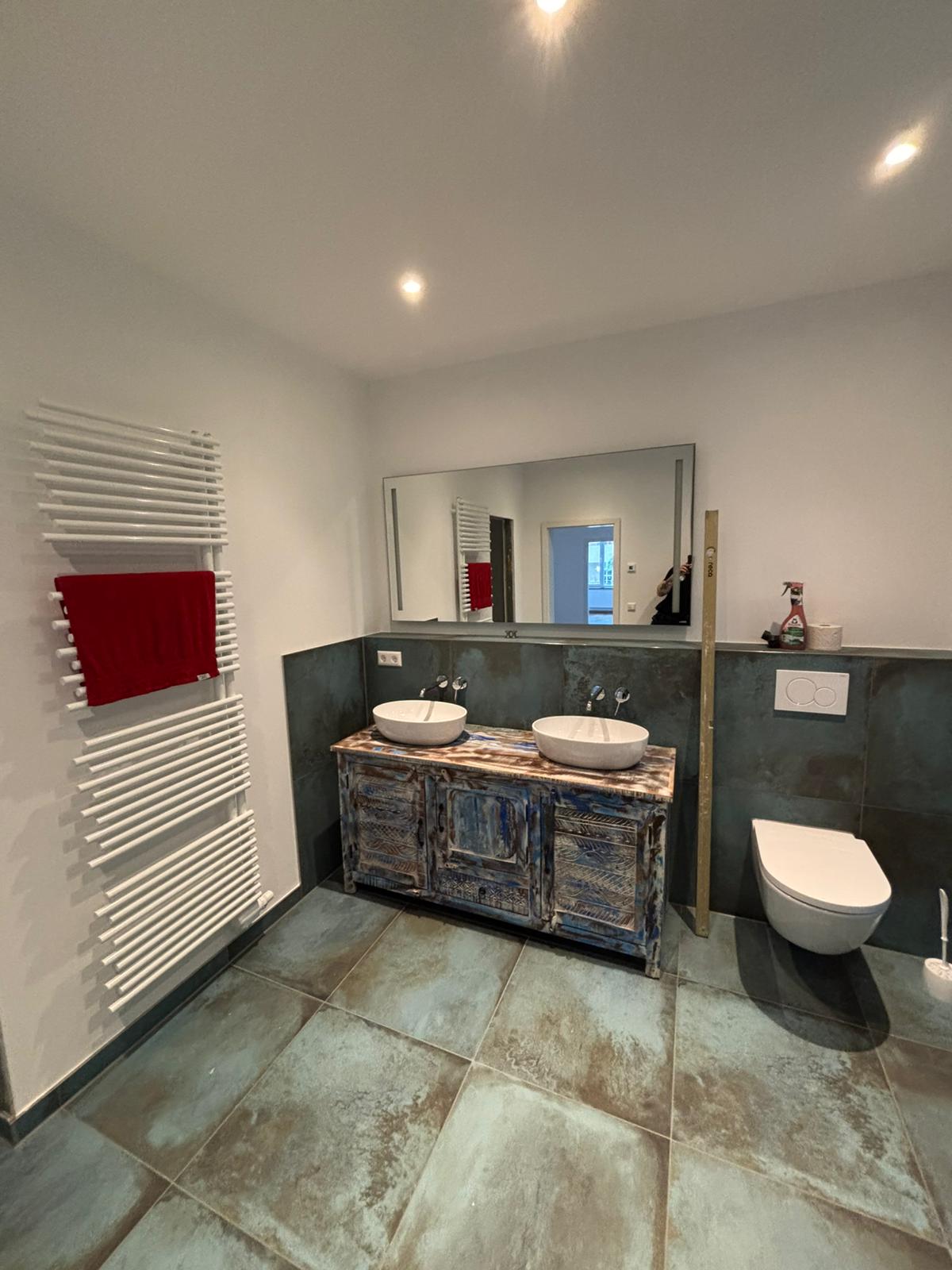 Ein modernes Badezimmer mit zwei Waschbecken, blauen Fliesen und einem roten Handtuch.
