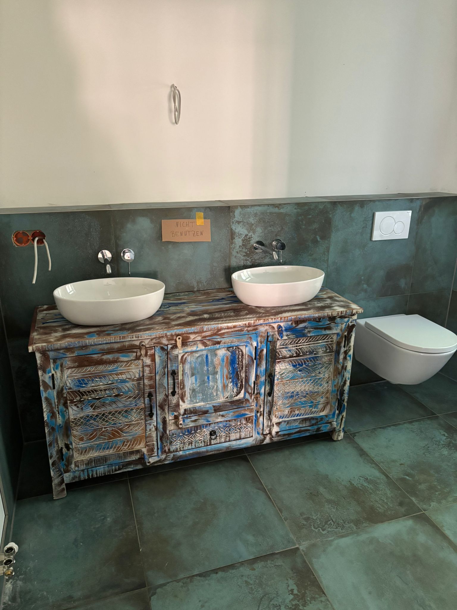 Zwei weiße Waschbecken auf rustikalem, verwittertem Holzschrank in einem Badezimmer mit grauen Fliesen.