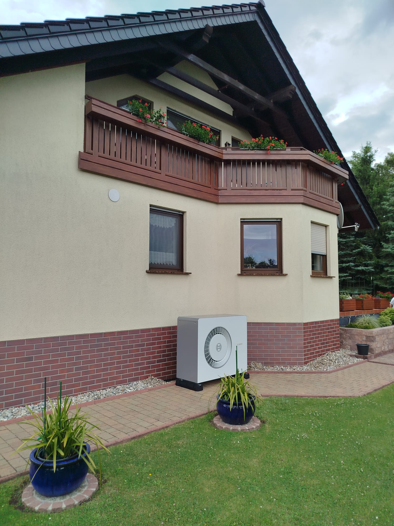 Gelbes Haus mit Dachboden, braunem Balkon und Lüftungseinheit im Garten.