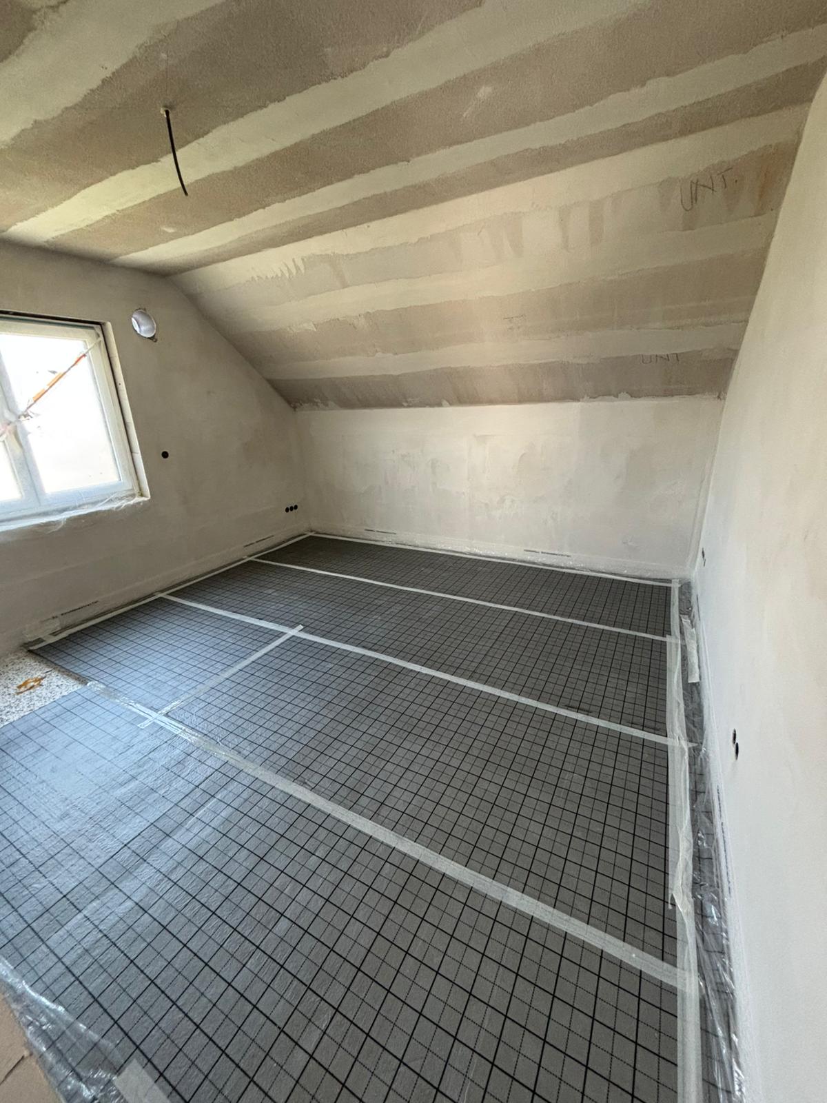 Renoviertes Zimmer mit Gitterboden und unfertigen Wänden in einem Dachgeschoss.