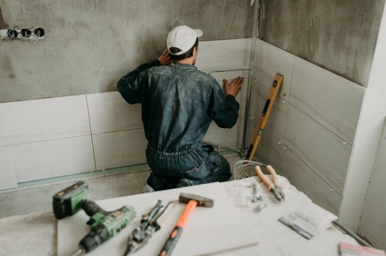 Der Handwerker bringt große Keramikfliesen an den Wänden des Badezimmers an und renoviert es.